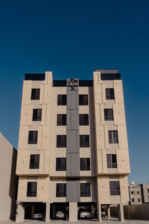 A modern multi-story building with a central entrance and parking garage. - Comfortable Two BR Home With Shared Garden (Madinah)