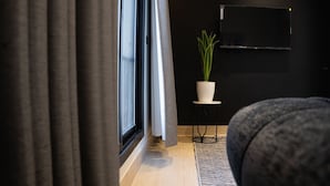 A modern living room with a large window, a potted plant, and a flat-screen TV mounted on the wall. - Comfortable Two BR Home With Shared Garden (Madinah)