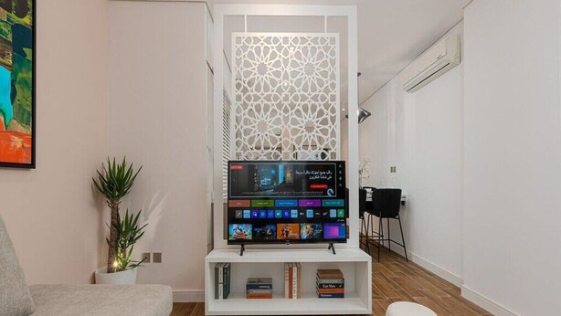 A modern living room with a flat-screen TV, a sofa, a coffee table, and a decorative screen. - Trendy & Cozy 1 BR Apartment in Almughrizat (Riyadh)