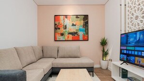 A modern living room with a sectional sofa, a wooden coffee table, a flat-screen TV, and a decorative wall piece. - Trendy & Cozy 1 BR Apartment in Almughrizat (Riyadh)