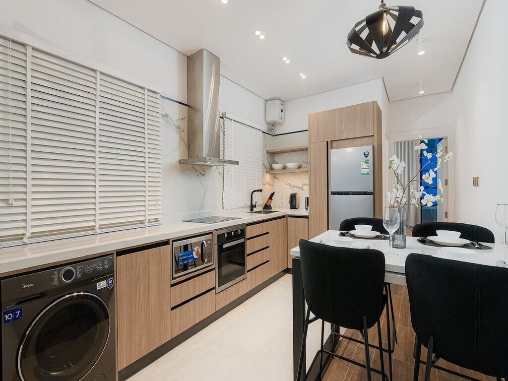 A modern kitchen with built-in appliances, a dining area with a table and chairs, and a large window with blinds.