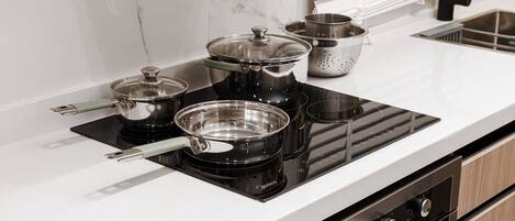 A kitchen with a black induction cooktop, stainless steel pots, and a colander.