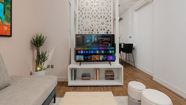 A modern living room with a flat-screen TV, a sofa, a coffee table, and a decorative screen. - Modern Comfort, Dedicated Desk, Free Parking (Riyadh)