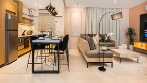A modern kitchen with a dining area, a sofa, and a floor lamp. - Elegant & Cozy Flat in Almughrizat (Riyadh)