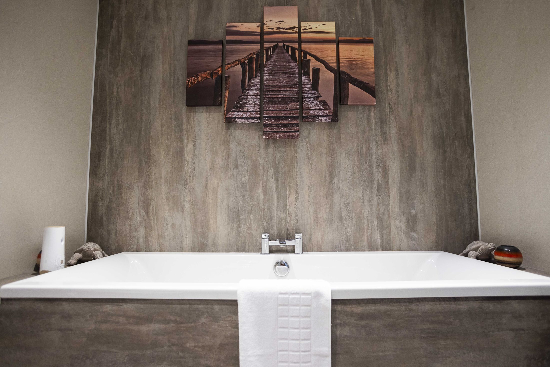 Une salle de bain moderne avec un plancher en bois, une baignoire blanche et une œuvre d’art murale représentant une jetée.