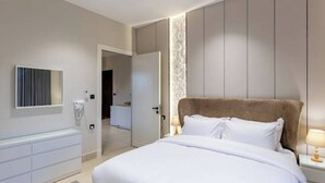 Una habitación de hotel moderna con una cama grande, una mesita de noche con lámpara, un armario y un baño visible a través de una puerta abierta.