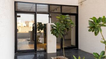 A modern building entrance with glass doors, a concrete pillar, and a small garden area with plants.