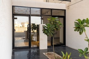 Une entrée moderne avec des portes en verre, un pilier en béton et un petit espace jardin agrémenté de plantes.