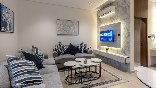 A modern living room with a grey sofa, striped pillows, a coffee table, a flat-screen TV, and a stone accent wall. - Free Parking, Near Prophet's Mosque & Quba Blvd (Madinah)