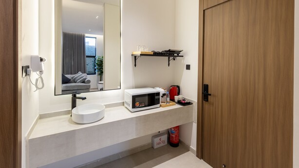 Een moderne badkamer met een wit wastafelmeubel, een spiegel, een magnetron en een plank met toiletartikelen.