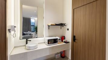 A modern bathroom with a white sink, a mirror, a microwave, and a shelf with toiletries.