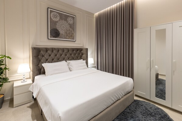 A neatly arranged bedroom with a tufted headboard, a large bed, a bedside table with a lamp, a wardrobe, and a framed artwork on the wall. - Free Parking, Near Prophet's Mosque & Quba Blvd (Madinah)