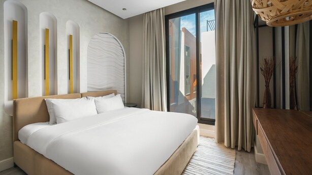 A modern hotel room with a large bed, a desk, and a view of the city through the window. - Two Bedroom Luxury Flat in Al-narjis (Riyadh)