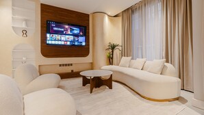 A modern living room with a curved sofa, a coffee table, and a flat-screen TV mounted on the wall. - Two Bedroom Luxury Flat in Al-narjis (Riyadh)