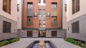 A modern building with a central courtyard featuring a water fountain, two large windows labeled 'B' and 'C', and decorative metal screens on the walls. - Two Bedroom Luxury Flat in Al-narjis (Riyadh)