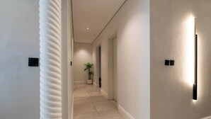 Un couloir au design moderne, avec un revêtement de sol de couleur claire, une plante en pot et un luminaire fixé au mur.