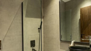 Een moderne badkamer met een douchecabine van glas, een wastafel met een zwarte wasbak en een houten deur op de achtergrond.