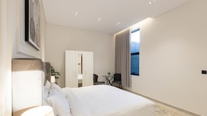 Een moderne hotelkamer met een groot bed, een nachtkastje met lamp, een kledingkast, een kleine tafel met stoelen en een raam met uitzicht op de omgeving.