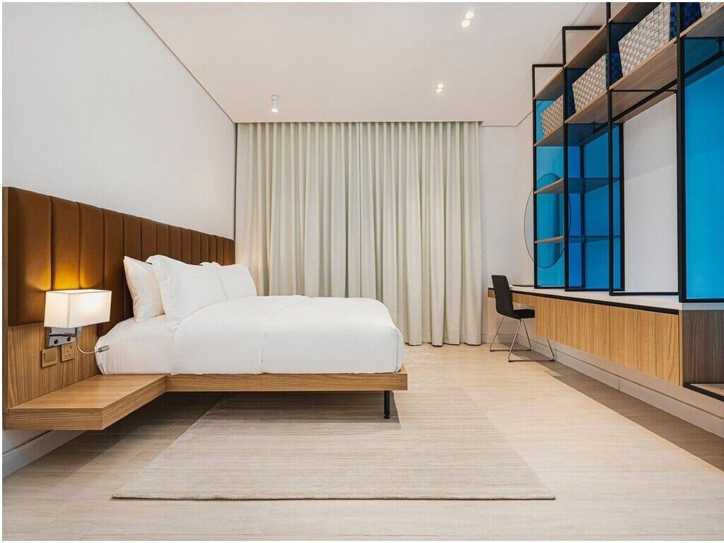 Una habitación de hotel moderna con cama, mesita de noche, lámpara y estante empotrado para televisión.