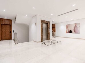 A spacious lobby with a marble floor, a wooden door, an elevator, and a staircase. - Stylish 1-br Apartment in Almughrizat (Riyadh)