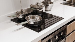 Una cocina moderna con placa de inducción, ollas de acero inoxidable y un colador.