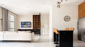 A modern kitchen with a built-in refrigerator, a dining area with bar stools, and a living room with a sofa and a flat-screen TV. - Exclusive Stay With Cinema, Wifi, Workspace (Riyadh)