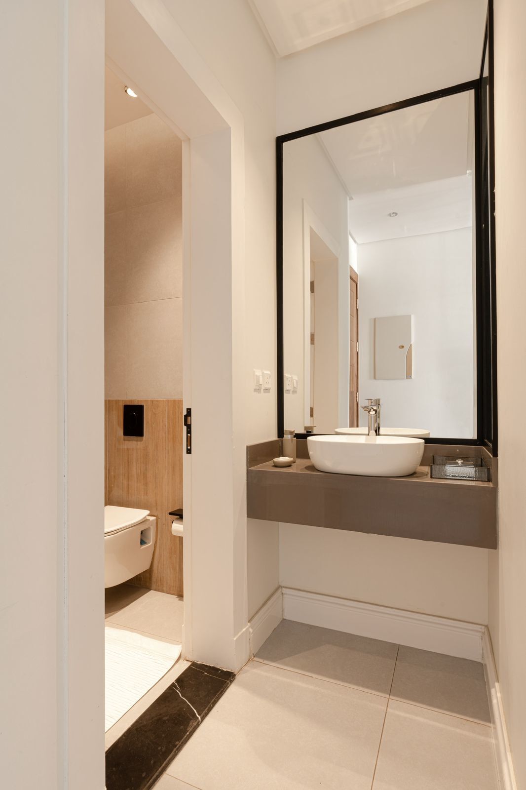 A modern bathroom with a large mirror, a white sink, and a toilet.
