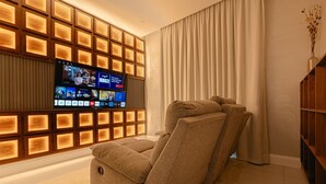 A modern living room with a large flat-screen TV mounted on a wooden panel wall, a beige sofa, and a wooden bookshelf. - Exclusive Stay With Cinema, Wifi, Workspace (Riyadh)