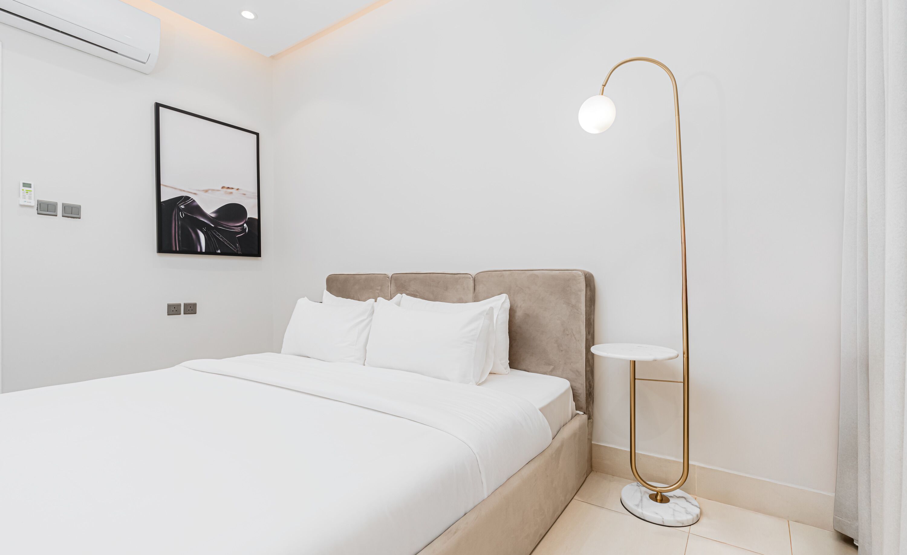 A modern bedroom with a bed, a bedside table, a floor lamp, and a framed picture on the wall.