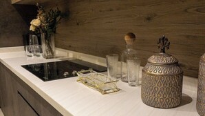 Une cuisine moderne avec un revêtement mural en bois, une plaque de cuisson à induction noire et un plan de travail blanc. On y trouve des récipients en verre décoratifs et un vase avec des fleurs sur le plan de travail.