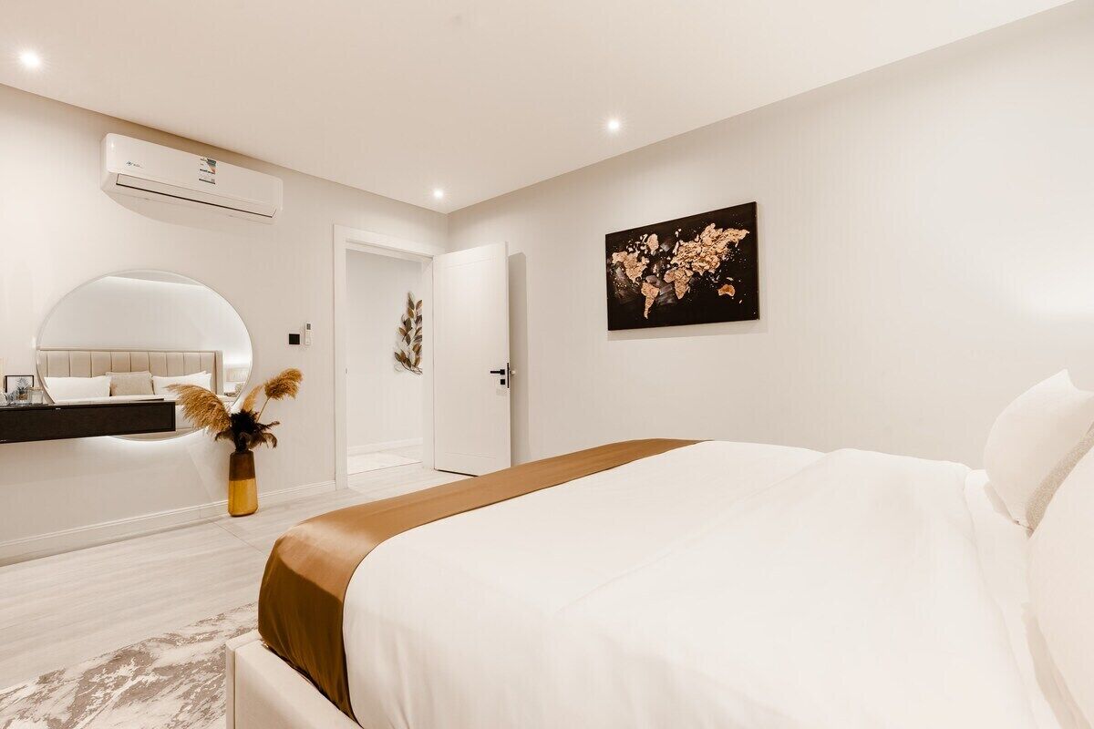 Une chambre d’hôtel moderne avec un grand lit, une table de chevet, un miroir et un climatiseur fixé au mur.