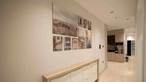A hallway with a modern kitchen in the background, a wooden console table, and a series of cityscape photographs on the wall. - Al Malqa Flat, Sleeps 4 With Free Parking (Riyadh)