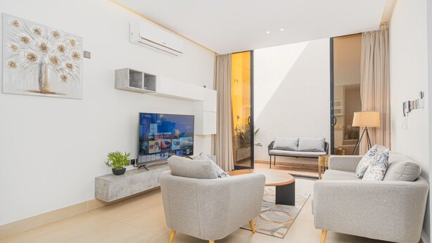 A modern living room with two grey armchairs, a coffee table, a flat-screen TV, and a painting on the wall. - Stylish & Modern Apartment in Alwadi (Riyadh)