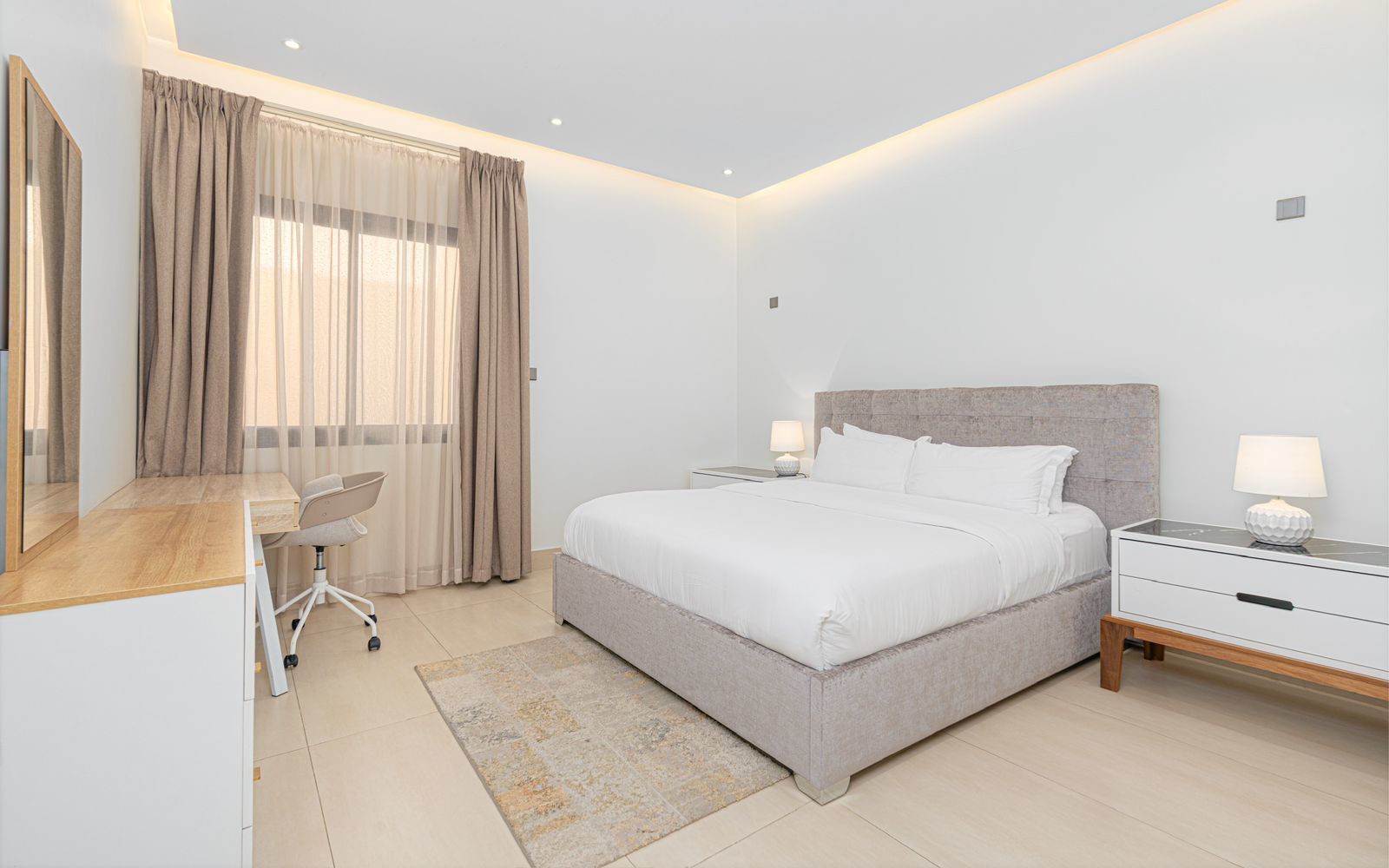 A modern bedroom with a large bed, bedside tables, a desk, and a chair.