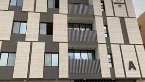 A modern building with a geometric facade, multiple balconies, and a prominent 'A' sign indicating a specific section or unit. - Stylish & Modern Apartment in Alwadi (Riyadh)