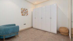 A room with a large white wardrobe, a blue sofa, and a decorative wall piece. - Stylish & Modern Apartment in Alwadi (Riyadh)