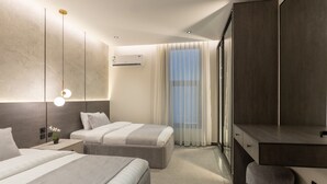 Quarto de hotel moderno com duas camas, uma escrivaninha, uma cadeira e uma janela grande com cortinas.