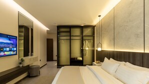 Una habitación de hotel moderna con una cama grande, un televisor montado en la pared, un vestidor y un baño con cabina de ducha de vidrio.