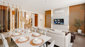 Un comedor moderno con una mesa blanca dispuesta para cuatro, un sofá y un televisor montado en la pared.
