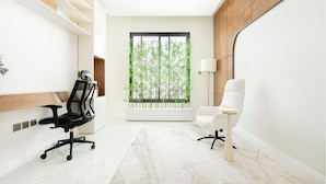 Un espacio de oficina moderno con una silla de oficina negra, una silla de oficina blanca, un ventanal con plantas de bambú y un suelo blanco.