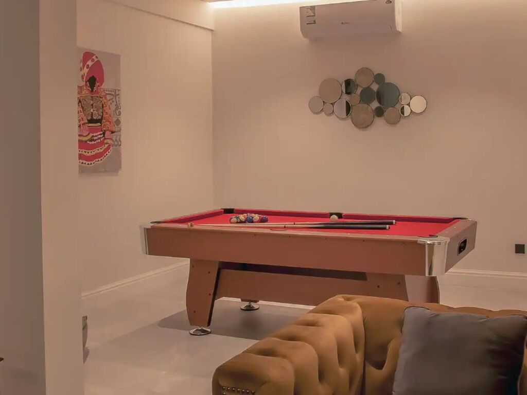 A pool table in a room with a cushioned seating area and a decorative wall piece.