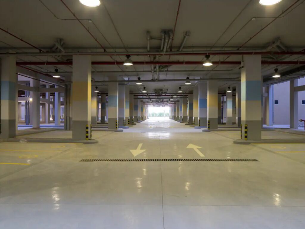 Un'ampia area di parcheggio interna con un percorso centrale e frecce direzionali sul pavimento.