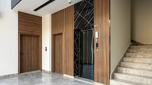 En moderne lobby med en trædør, en sort elevator og en marmortrappe.