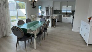 Une cuisine spacieuse avec des meubles blancs, un réfrigérateur en acier inoxydable et un coin repas comprenant une table et des chaises en verre.