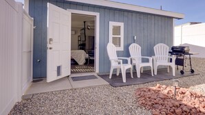 Een klein, laag gebouw met een openstaande deur naar een kamer. Daarbuiten staan twee witte Adirondack-stoelen en een barbecue.