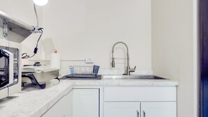 Een kleine keuken met een ingebouwde magnetron, een gootsteen met een moderne kraan en een afwasschuur.