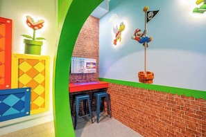 Quarto com parede de tijolos, decoração temática do Mario, escrivaninha e dois banquinhos.