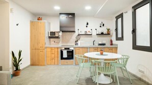 A modern kitchen with wooden cabinets, a built-in oven, a microwave, and a round dining table with green chairs. - Private Terrace Dishwasher 3 Bedrooms (Barcelona)
