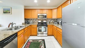 A modern kitchen with wooden cabinets, stainless steel appliances, granite countertops, and a tiled backsplash. - Golf Views: Kissimmee Condo on Reunion Course (Kissimmee)