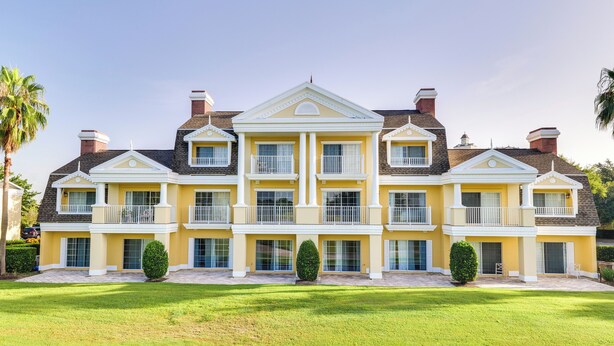 A large, yellow multi-story building with a symmetrical facade, multiple balconies, and a well-maintained lawn in front. - Golf Views: Kissimmee Condo on Reunion Course (Kissimmee)